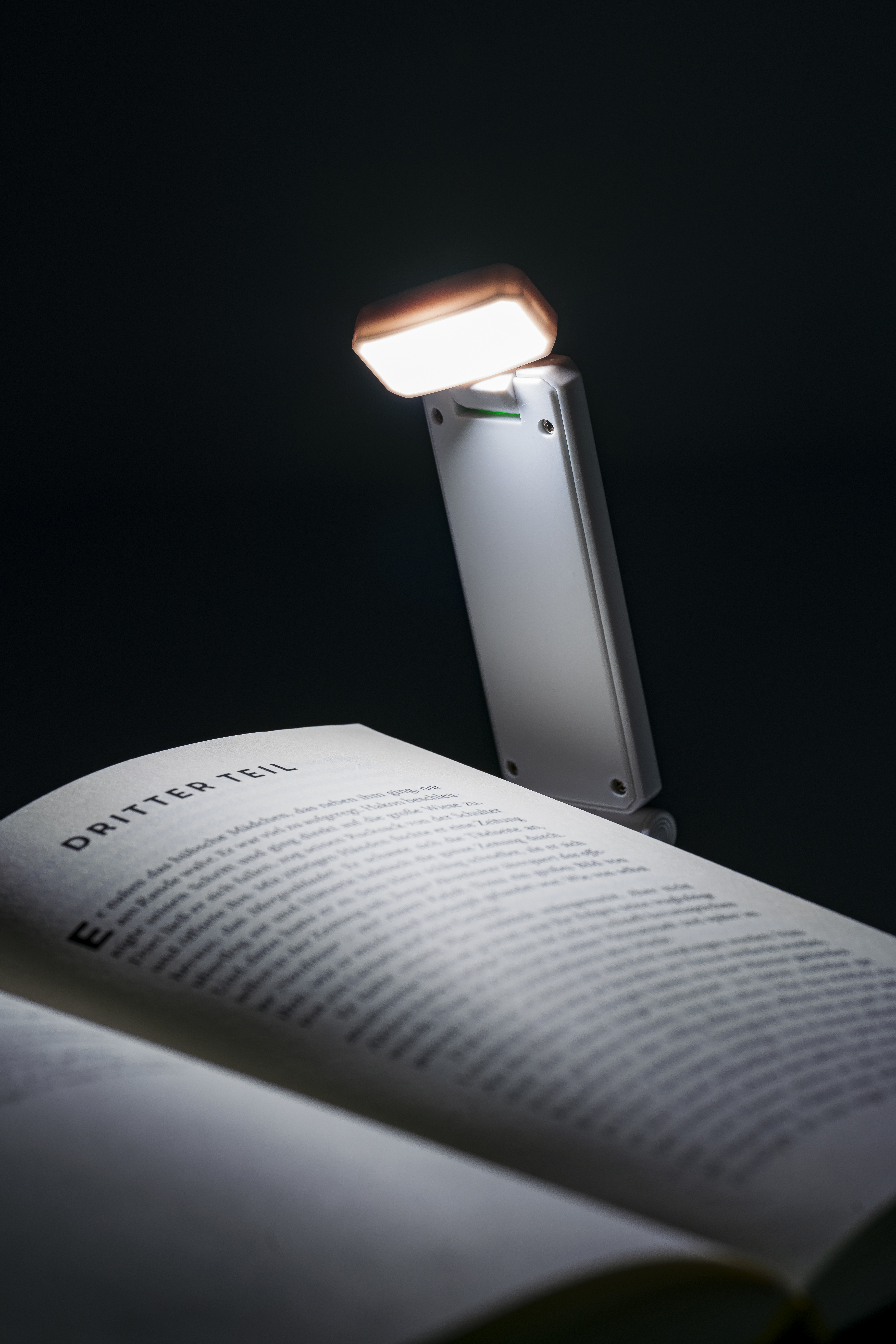 Weiße, klappbare Leseleuchte im Hosentaschenformat mit Clip , der in einen Buchrücken geschoben ist.