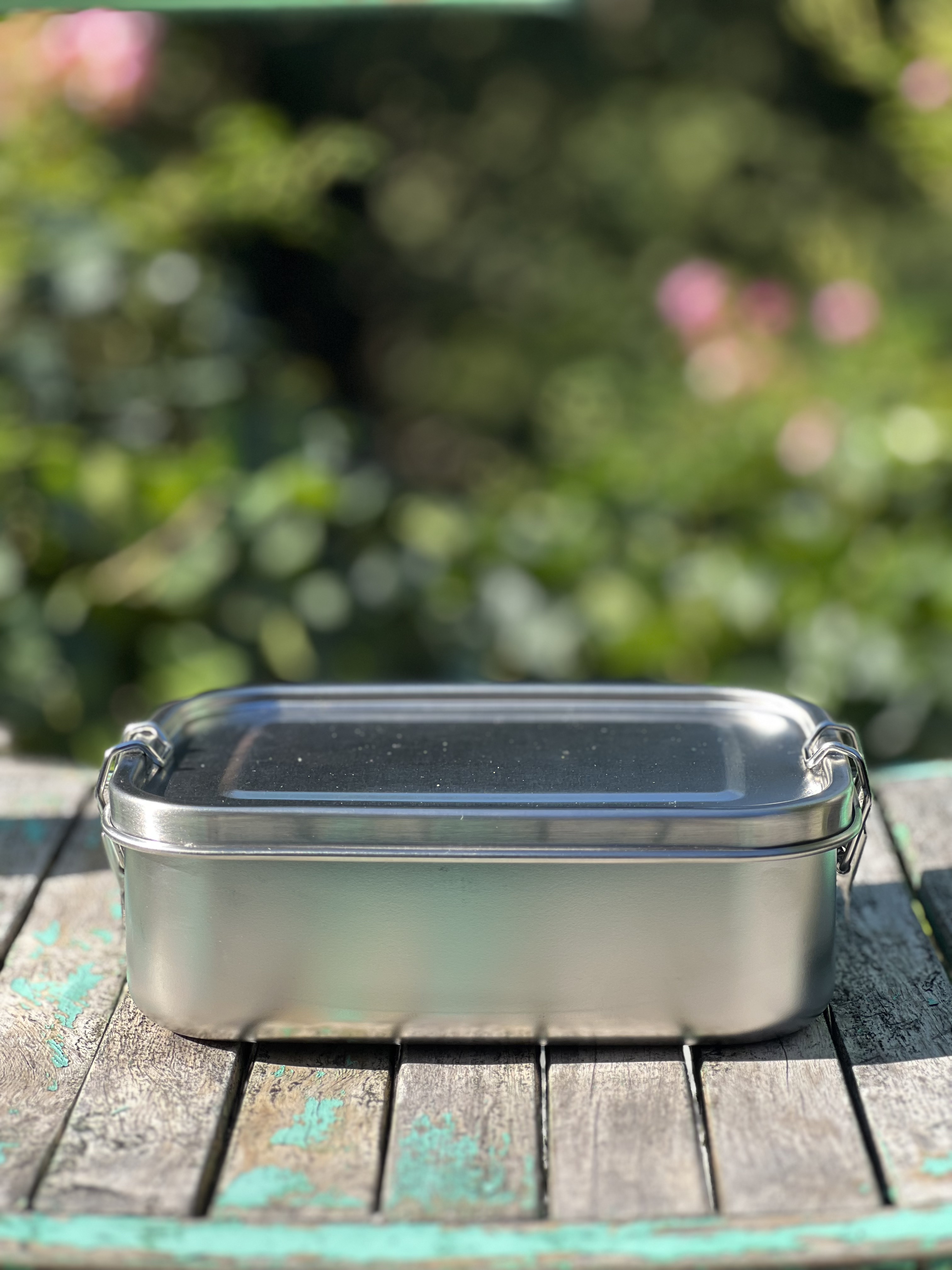 Umweltfreundliche Lunchbox mit Clip aus Edelstahl, auf einer Bank dargestellt.