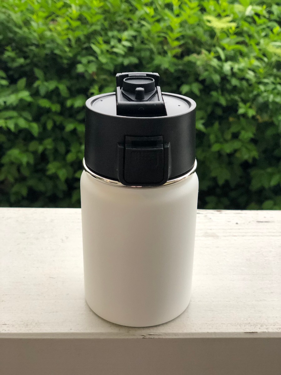 Weisser Kaffeebecher to go aus doppelwandigem Edelstahl mit Einhand Click-Verschluss 350 ML, dargestellt im Freien.